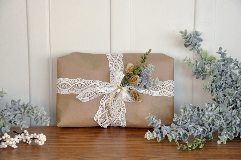 May include: A brown paper gift package tied with white lace ribbon and decorated with a sprig of dried greenery.