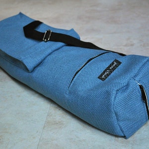 May include: A blue yoga mat bag with a black strap and zipper. The bag has a small pocket on the front with a black label that says "Yoga Soul".