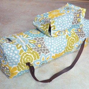 May include: A blue and yellow floral print duffel bag with a brown strap. The bag has a zippered pocket on the side and a smaller, separate compartment on top.