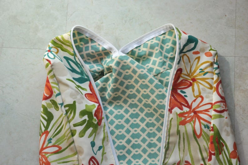 May include: A white fabric with a floral pattern in shades of orange, green, and teal. The fabric is folded in half, revealing a turquoise and white geometric pattern on the inside.