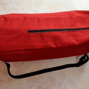 Pu&ograve; includere: Una borsa per tappetino da yoga rossa con una cerniera nera e una tracolla nera regolabile.