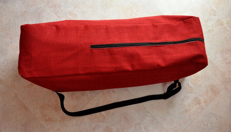 Pu&ograve; includere: Una borsa per tappetino da yoga rossa con una cerniera nera e una tracolla nera regolabile.