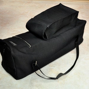 May include: A black canvas duffel bag with a smaller black canvas pouch attached to the top. The bag has a zippered pocket on the side and a long strap.