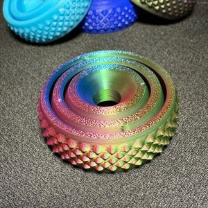 May include: A multi-layered, iridescent, rainbow-colored, circular object with a textured surface. The object has a central hole and is made of plastic.