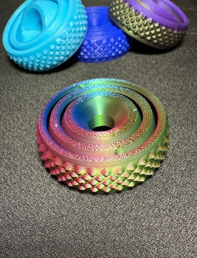May include: A multi-layered, iridescent, rainbow-colored, circular object with a textured surface. The object has a central hole and is made of plastic.