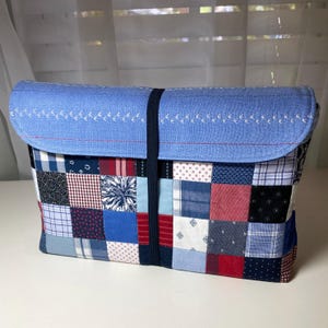 May include: A patchwork laptop sleeve featuring a blue flap with white bird embroidery and a red stitched border. The body is a mix of red, white, and blue patterned fabric squares, secured with a navy elastic band.