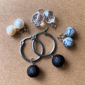 May include: A set of three ceramic mugs with a speckled, matte finish. The mugs are in shades of cream, light gray, and dark gray. Each mug has a simple, minimalist design and a rounded handle. The mugs are likely for coffee or tea.