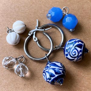 May include: An assortment of earrings with various designs. There are two pairs of silver hoop earrings, each with different dangling beads. One pair has white, ridged beads, another has clear, faceted beads, and the others have blue and white patterned beads.