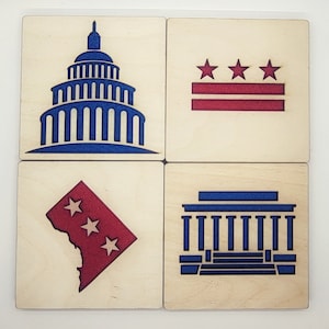 May include: Four wooden coasters with laser-cut designs representing Washington, D.C. The coasters feature a blue and white Capitol Building, a red and white flag with three stars, a red and white outline of the District of Columbia, and a blue and white building with columns.