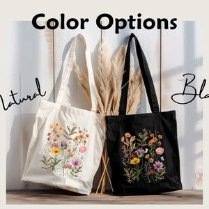 Natural colored canvas tote and black canvas tote hung next to each other. Cottage core style wildflowers of yellow, orange, purple, and pink are center arranged in a rectangular shape and printed on the tote.