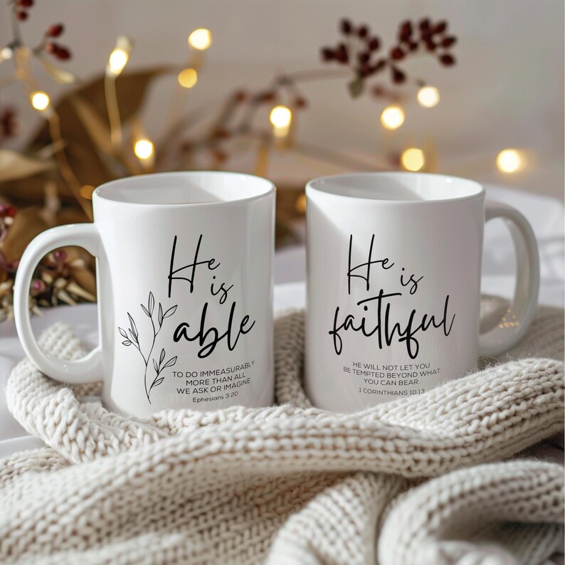 K&ouml;nnte beinhalten: Zwei wei&szlig;e Keramikbecher mit schwarzer Beschriftung. Der Becher links sagt "Er ist f&auml;hig" mit der Schrift Eph 3,20. Der Becher rechts sagt "Er ist treu" mit der Schrift 1 Kor 10,13.