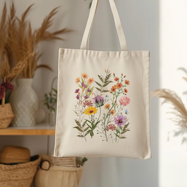 Op de afbeelding: Een witte canvas tote bag met een bloemenprint met verschillende kleurrijke bloemen, waaronder gele, roze, paarse en oranje.