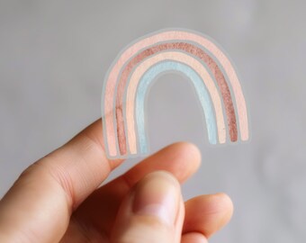 Op de afbeelding: Een transparante sticker met een aquarel regenboogontwerp. De regenboog heeft vier kleurbanden: een licht perzik, een donkerder perzik, een lichtblauw en een donkerder blauw.