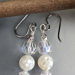 May include: A pair of dangle earrings featuring silver-toned hooks, small decorative metal spacers, faceted iridescent clear crystal beads, and round white mother-of-pearl beads with a checkered pattern, finished with small clear crystal bicones.