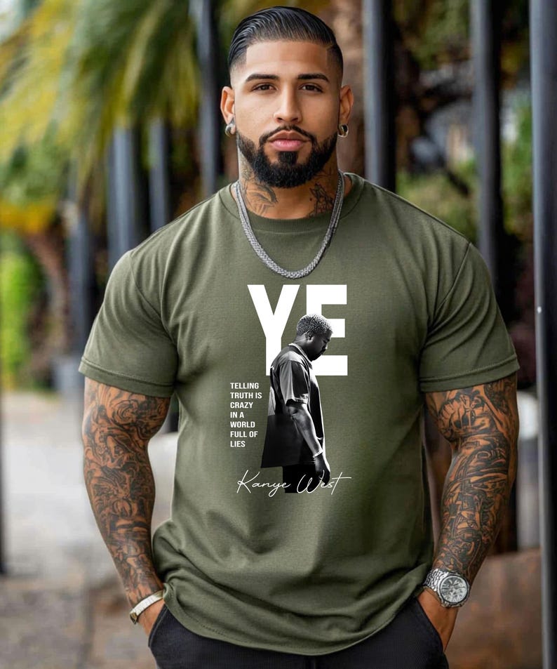 May include: Olive green t-shirt featuring the word "YE" in white block letters. Below the text is a black and white image of a person, with the text "TELLING TRUTH IS CRAZY IN A WORLD FULL OF LIES" and "Kanye West" in a script font.