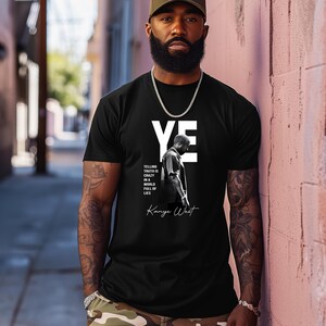May include: Black t-shirt with the word "YE" in white block letters and a black and white image of a person. The text "TELLING TRUTH IS CRAZY IN A WORLD FULL OF LIES" and "Kanye West" are also printed on the shirt.