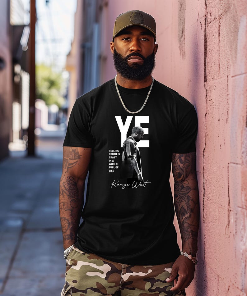 May include: Black t-shirt with the word "YE" in white block letters and a black and white image of a person. The text "TELLING TRUTH IS CRAZY IN A WORLD FULL OF LIES" and "Kanye West" are also printed on the shirt.