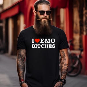 Può includere: T-shirt nero con la scritta "I ❤️ EMO BITCHES" in lettere bianche e un cuore rosso. La persona che indossa la maglietta ha una lunga barba e occhiali da sole.