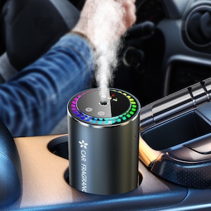 May include: A black car air freshener with a rainbow light ring and a white mist coming out of the top. The air freshener says "CAR FRAGRANC" on the side.