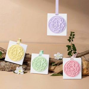 May include: Five white square cards with a floral design in the center. The cards are hanging from a string or ribbon. The flowers are in shades of yellow, green, pink, and purple.