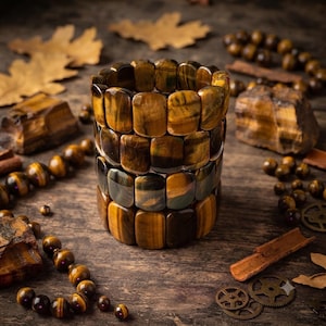May include: A stack of four bracelets made of rectangular tiger's eye beads. Each bead displays a chatoyant golden-brown and dark brown banded pattern. The bracelets are arranged vertically, showcasing the polished, smooth surface of the natural stone segments linked together in a continuous circular form.