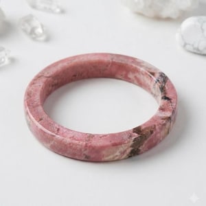 Peut inclure: Un bracelet jonc circulaire en pierre de rhodonite polie, présentant une surface lisse et arrondie avec un motif naturel marbré composé de veines rose poudré, rose tendre et gris anthracite foncé sur toute la structure de la pierre.
