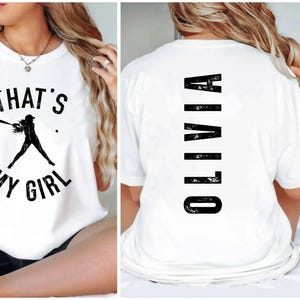 May include: White t-shirt with a black graphic of a baseball player and the text "That's My Girl". The back of the shirt has the name "Olivia" printed vertically in black.
