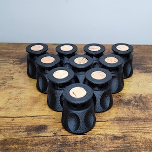 Può includere: Una collezione di barattoli neri, strutturati, con tappi in sughero disposti su una superficie di legno. I barattoli hanno una forma arrotondata con un motivo strutturato. I tappi in sughero sono circolari e marrone chiaro.