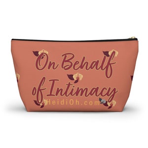 May include: A peach-colored zippered pouch with the text "On Behalf of Intimacy" in burgundy script. The pouch features floral accents and the website HeidiOh.com. The bag is designed to stand upright.