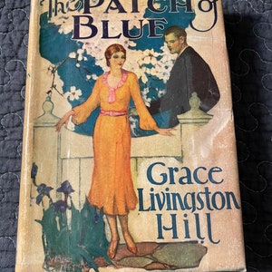 May include: The Patch of Blue book cover features a couple standing in front of a white picket fence. The woman is wearing a yellow dress and the man is wearing a dark suit. The book title is in blue and white lettering and the author's name is Grace Livingston Hill.