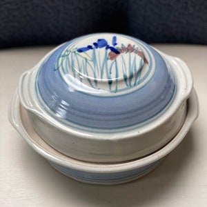 May include: A blue and white ceramic casserole dish with a floral design. The dish has a lid and two handles.