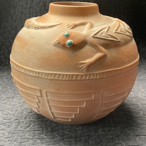 May include: A terracotta vase with a raised design of a lizard with turquoise eyes. The vase has a geometric pattern around the bottom.
