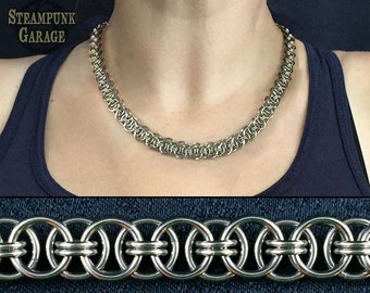 May include: A silver chain necklace made of interlocking rings. The chain is about 18 inches long and has a delicate, intricate design. The necklace is shown on a person's neck, but the person's face is not visible.