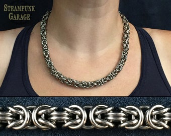May include: A silver chain necklace made of interlocking rings. The chain is thick and has a polished finish. The necklace is shown on a person's neck.