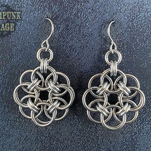 May include: A pair of silver earrings with a geometric, flower-like design. Each earring is made of multiple interconnected rings.