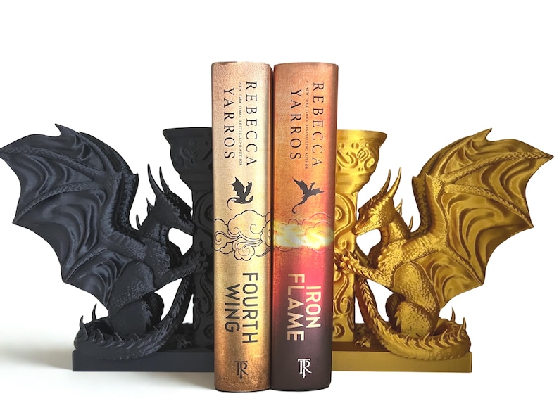 Op de afbeelding: Draakvormige boekensteunen in zwart en goud. De boekensteunen tonen gedetailleerde drakenbeelden met uitgespreide vleugels. Twee boeken, "Fourth Wing" en "Iron Flame" van Rebecca Yarros, staan tussen de boekensteunen. De boeken hebben gouden en oranje covers.