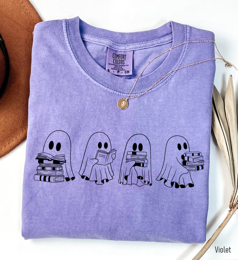 May include: A purple t-shirt with a graphic of four ghosts holding stacks of books. The text "Comfort Colors" is on the tag.