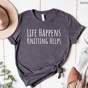 May include: Dark grey heather t-shirt with the text "Life Happens Knitting Helps" in white.