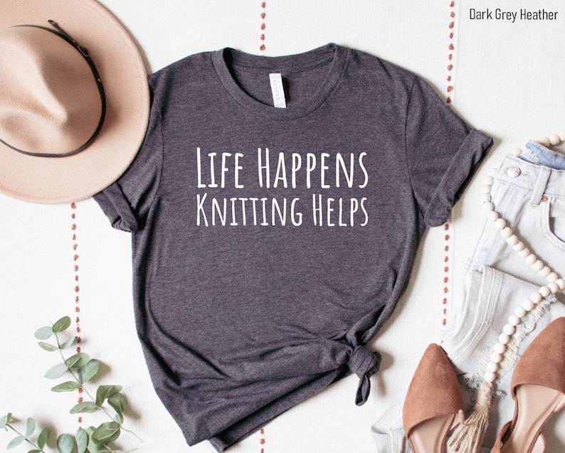 May include: Dark grey heather t-shirt with the text "Life Happens Knitting Helps" in white.