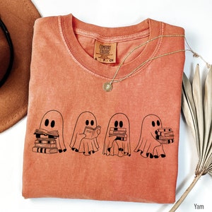 May include: A burnt orange t-shirt with a graphic of four ghosts holding stacks of books. The text "Comfort Colors" is visible on the tag.