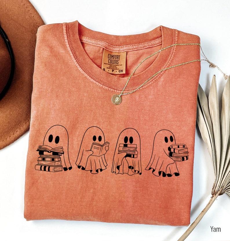 May include: A burnt orange t-shirt with a graphic of four ghosts holding stacks of books. The text "Comfort Colors" is visible on the tag.