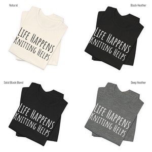May include: Four folded t-shirts in different colors: natural, black heather, solid black blend, and deep heather. Each shirt features the text "LIFE HAPPENS KNITTING HELPS" in white.