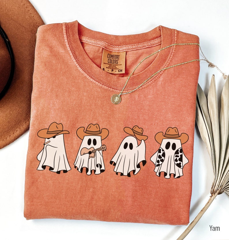 May include: A burnt orange t-shirt with a graphic of four ghosts wearing cowboy hats. The ghosts are playing musical instruments. The text "COMFORT COLORS" is on the tag.