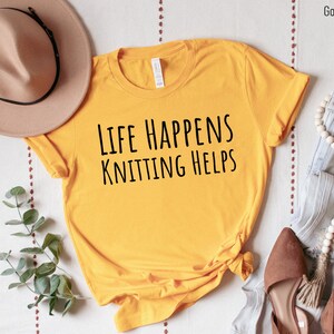 May include: A yellow t-shirt with the text "Life Happens Knitting Helps" in black lettering.