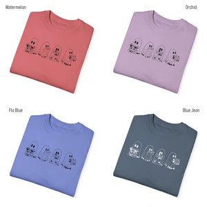 May include: Four folded t-shirts in different colors: watermelon, orchid, flo blue, and blue jean. Each shirt features a graphic of three ghosts reading books.