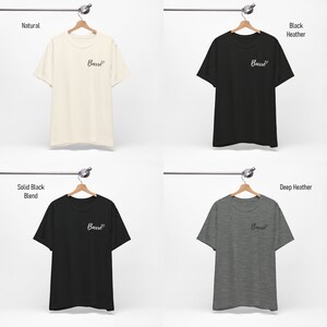 May include: Four t-shirts hanging on hangers, each in a different color: natural, black heather, solid black blend, and deep heather. Each shirt has the word "Barre" printed on the front in a cursive font with a heart symbol.