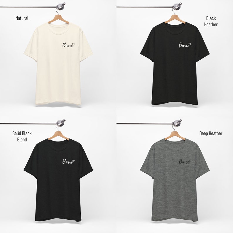 May include: Four t-shirts hanging on hangers, each in a different color: natural, black heather, solid black blend, and deep heather. Each shirt has the word "Barre" printed on the front in a cursive font with a heart symbol.