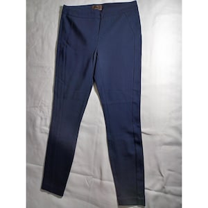 May include: Navy blue pants with a tailored fit. The pants have a flat front, a concealed closure, and a subtle seam detail running down the front of each leg. The fabric appears to be a smooth, woven material. A small, brown accent is visible at the waistband.