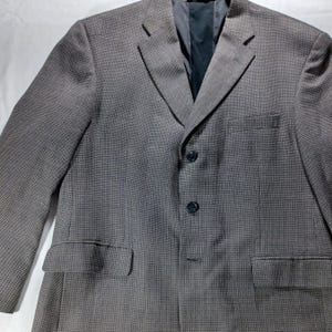 May include: A gray blazer with a subtle textured pattern. The blazer has a notched lapel, three black buttons, and two front pockets. The interior lining is a dark gray color.