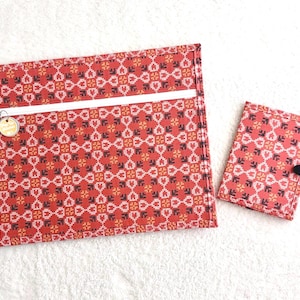 Può includere: Un set di tessuto rosso fantasia, composto da una grande pochette con cerniera e un portafoglio più piccolo abbinato. Il motivo include forme geometriche bianche, nere e gialle. La pochette ha una cerniera bianca e un piccolo ciondolo dorato.